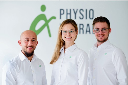 Das Bild zeigt drei Mitarbeitende vor einer hellen Wand mit dem Logo und dem Schriftzug „alpha physio therapie“ im Hintergrund. Links steht ein Mann mit Glatze und kurzem dunklem Bart. Er trägt ein weißes Hemd mit kleinem grünem Logo auf der Brust und lächelt leicht in die Kamera. In der Mitte steht eine Frau mit langen, hellblonden Haaren und einer Brille. Auch sie trägt ein weißes Hemd mit grünem Logo. Sie lächelt freundlich und steht aufrecht zwischen den beiden Kollegen. Rechts steht ein Mann mit kurzen braunen Haaren, Bart und Brille. Er trägt ebenfalls ein weißes Hemd mit grünem Logo und lächelt in die Kamera. Alle drei wirken professionell und freundlich. Der Hintergrund ist hell und schlicht gestaltet.