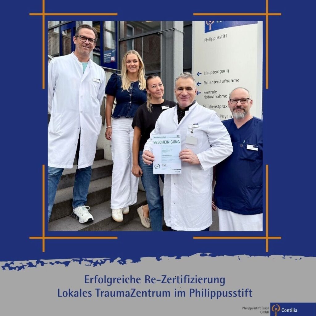 Fünf Mitarbeitende des Philippusstifts stehen vor dem Haupteingang des Krankenhauses. Zwei Personen tragen weiße Arztkittel, eine Person blaue Bereichskleidung, zwei weitere sind in ziviler Kleidung. Der Arzt in der Bildmitte hält die Bescheinigung zur erfolgreichen Re-Zertifizierung als Lokales TraumaZentrum in den Händen. Im Hintergrund ist das Wegweiser-Schild des Philippusstifts zu sehen. Das Bild ist in ein blaues Layout eingebettet. Darunter steht: „Erfolgreiche Re-Zertifizierung – Lokales TraumaZentrum im Philippusstift“.